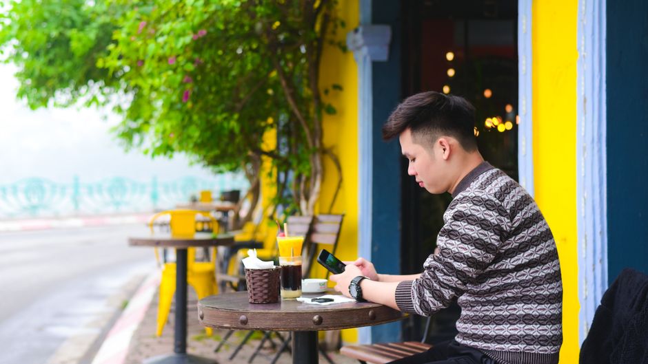 Man sitting at an outdoor cafe, engrossed in his smartphone on a calm day.